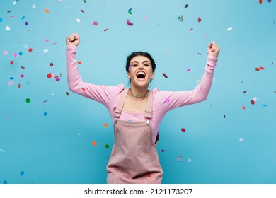 Excited Woman Shouting And Showing Triumph Gesture Under Falling Confetti On Blue Background