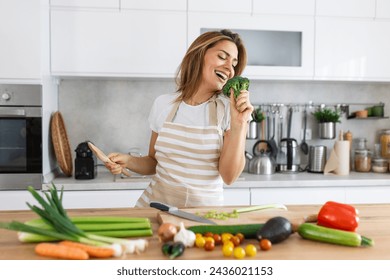 Excited woman singing and dancing in modern kitchen at home, happy woman holding spatula as microphone, dancing, listening to music, having fun with kitchenware, preparing breakfast - Powered by Shutterstock