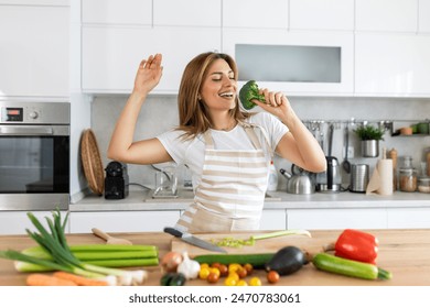 Excited woman singing and dancing in modern kitchen at home, happy woman holding broccoli as microphone, dancing, listening to music, having fun with kitchenware, preparing breakfast - Powered by Shutterstock