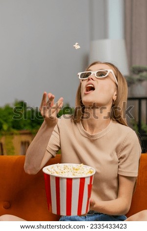 Excited woman sits on sofa throws eating popcorn, tries to catch with mouth . Girl in 3D glasses watching interesting tv serial, sport game, film, online social media movie content at home. Vertical