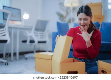 Excited woman unpacking boxes in new office, setting up desk for startup. Bright modern interior with blue and red furniture - Powered by Shutterstock