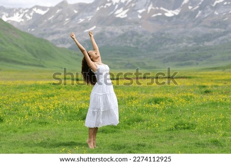 Excited woman in white dress raising arms in nature