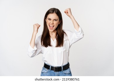 Excited young adult woman reacting to win, surprise news, screaming and cheering, triumphing, achieve goal and celebrating, standing over white background - Powered by Shutterstock