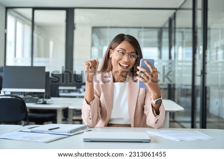 Excited young African American business woman winner executive looking at cell phone celebrating financial success, happy about professional results receiving mobile message on cellphone in office.