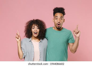 Excited young african american couple in love woman man, gray green casual clothes posing holding index finger up with great new idea strategy isolated on pastel pink color background studio portrait
