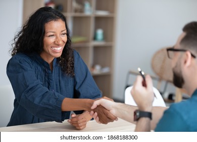 Excited Young African American Female Woman Shake Hand Of Male Recruiter Or Employer At Office Meeting. Happy Diverse Business Partners Handshake Close Deal Make Agreement. Acquaintance Concept.