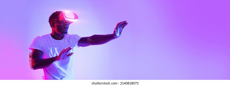 Excited young African American guy using VR glasses, touching something invisible at copy space, millennial black man experiencing virtual reality adventure on neon studio background, panorama banner - Shutterstock ID 2140818073