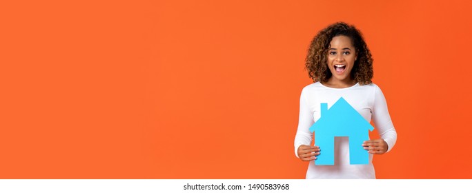 Excited young African American woman holding house model isolated on orange banner background with copy space for real estate concept