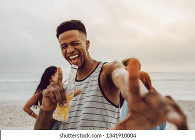 Excited young african man with beer on the beach with friends at the back. Smiling male with group of friends in background at beach. - Powered by Shutterstock