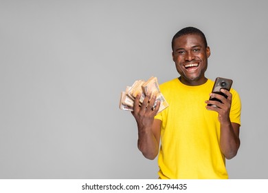 Excited Young African Man Holding Cash And Using His Phone Rejoicing