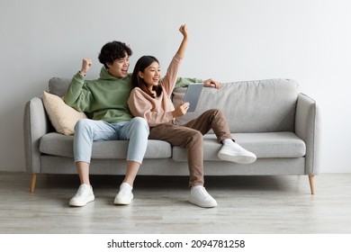 Excited young Asian couple sitting on couch with tablet pc, celebrating online win, great deal or business success at home, free space. Millennial spouses enjoying big sale in web store - Shutterstock ID 2094781258