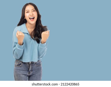 Excited young asian female with raised hands celebrating success Portrait cheerful positive asian woman with raised hands and fists open mouth Girl get happy Pastel blue background, copy space