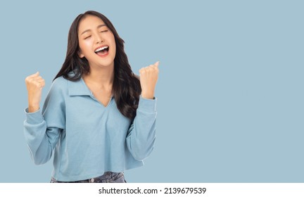 Excited Young Asian Female With Raised Hands Celebrating Success Portrait Cheerful Positive Asian Woman With Raised Hands And Fists Open Mouth Girl Get Happy, Enjoy Life Isolated On Blue Copy Space