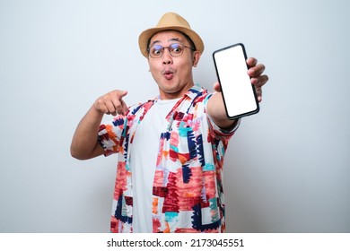 Excited Young Asian man wearing casual beach shirt shock showing phone screen at camera pointing at white phone screen, isolated on white background - Shutterstock ID 2173045551