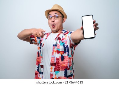 Excited Young Asian man wearing casual beach shirt shock showing phone screen at camera pointing at white phone screen, isolated on white background - Powered by Shutterstock