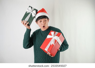 Excited young asian man wearing santa clause hat and green long sleeved sweater is carrying large gift box with ribbon, isolated over white background. Concept for Christmas Holiday and New Year Party - Powered by Shutterstock