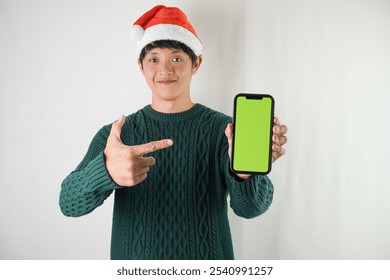 Excited young asian man wearing santa clause hat and green long sleeved sweater is showing smartphone green screen, isolated over white background. Concept for Christmas Holiday and New Year Party - Powered by Shutterstock