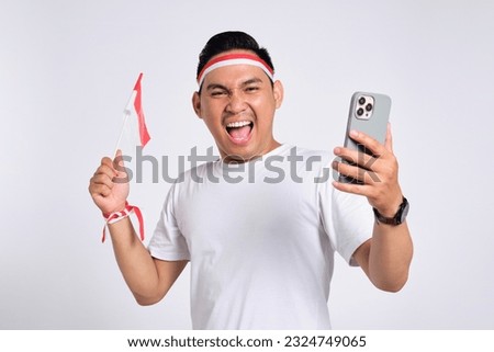 Excited young Asian men celebrate Indonesian independence day on 17 August while holding the Indonesian flag and mobile phone isolated over white background