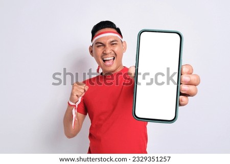 Excited young Asian men celebrate Indonesian independence day on 17 August while holding smartphone with blank screen isolated over white background