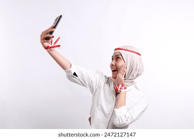 Excited young Asian muslim woman waving her hand while making video call on smartphone isolated over white background. Celebrate Indonesian independence day on 17 August - Powered by Shutterstock