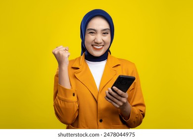 Excited young Asian woman holding mobile phone and gesturing yes, celebrating success, raising clenched fist isolated on yellow background - Powered by Shutterstock