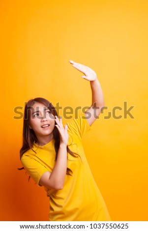 Excited young Asian woman look up in yellow dress on yellow background