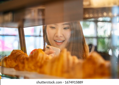 Excited Young Asian Woman Looking Croissants On The Shelf At Bakery Shop.