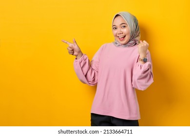 Excited Young Asian Woman In Pink Shirt Pointing Fingers At Copy Space On Yellow Background