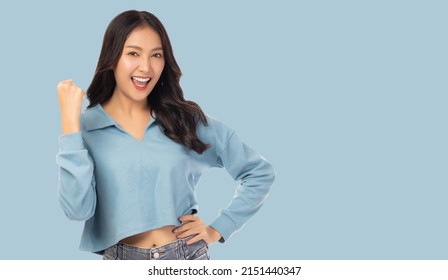 Excited young asian woman with raised hand celebrating success Portrait cheerful positive asian female with raised hands and fist open mouth Girl get happy enjoy life blue pastel color background 
