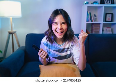 Excited young Asian woman watching TV and cheering sport games competition with laugh victory on sofa at home. - Shutterstock ID 2174856125