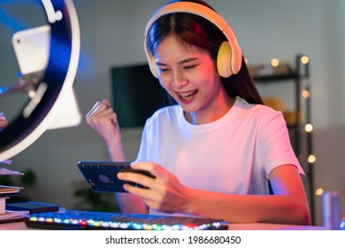 Excited Young Asian Woman Wearing Headset And Playing Online Game On Smartphone With Live Broadcasting On Internet.