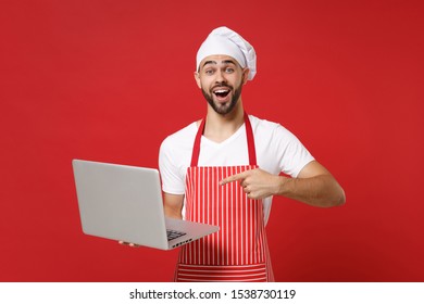 Excited young bearded chef cook or baker man in striped apron t-shirt toque chefs hat isolated on red background. Cooking food concept. Mock up copy space. Pointing index finger on laptop pc computer - Powered by Shutterstock