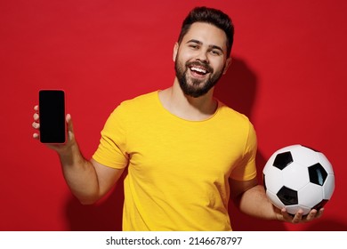 Excited Young Bearded Man Football Fan In Yellow T-shirt Support Favorite Team Hold Soccer Ball Mobile Cell Phone With Blank Screen Workspace Area Isolated On Plain Dark Red Background Studio Portrait