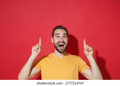 Excited young bearded man guy in casual yellow t-shirt posing isolated on red wall background studio portrait. People sincere emotions lifestyle concept. Mock up copy space. Pointing index fingers up