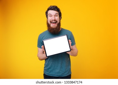 Excited young bearded man showing white blank of tablet screen and lookiing at camera  - Shutterstock ID 1333847174