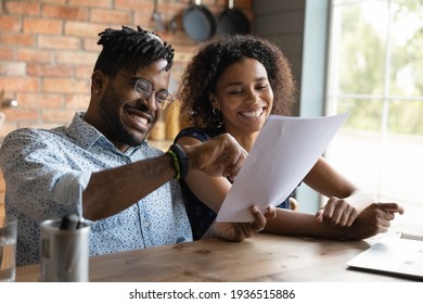 Excited young black husband wife read paper loan mortgage contract life insurance policy satisfied with good conditions offered. Smiling african couple receive tax refund letter glad to get money back - Shutterstock ID 1936515886