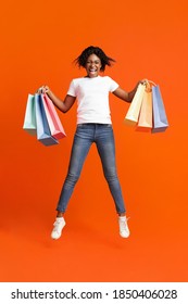 Excited Young Black Lady With Colorful Shopping Bags Screaming And Jumping Up Over Orange Studio Background. Happy African American Woman Holding Purchases, Shopping During Sale Season