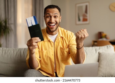 Excited Young Black Man With Passport And Plane Ticket Gesturing YES, Using Laptop To Buy Hot Tour At Web Travel Agency From Home. Online Tickets Booking, Hotel Reservation, Summer Vacation