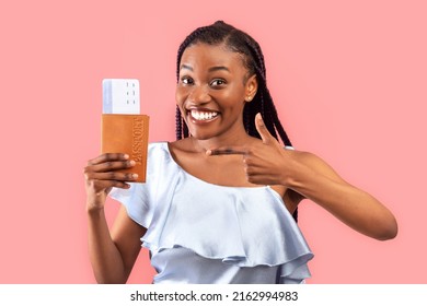 Excited Young Black Woman Pointing At Passport And Plane Tickets, Going On Abroad Vacation, Traveling Overseas Over Pink Studio Background. Tourism, Summer Holidays Concept