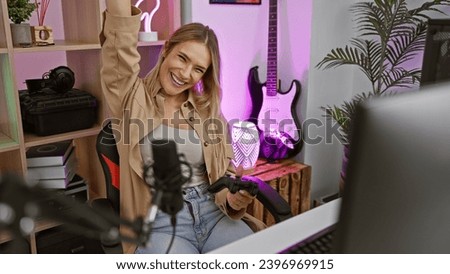 Excited young blonde streamer woman's night of victory, joyously playing video game with joystick, celebrating in cool home gaming room, streaming live for her internet fans