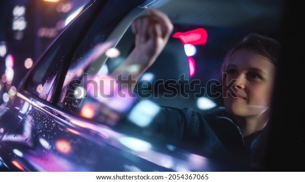Excited Young Boy is\
Sitting on Backseat of a Car, Commuting Home at Night. Looking Out\
and Drawing on the Taxi Window while Riding the City Street with\
Working Neon Signs.