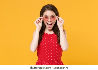 Excited young brunette woman 20s in red summer dress, eyeglasses posing isolated on yellow wall background studio portrait. People emotions lifestyle concept. Mock up copy space. Keeping mouth open