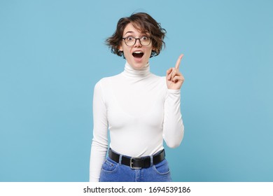 Excited young brunette woman girl in casual white clothes, eyeglasses posing isolated on pastel blue background. People lifestyle concept. Mock up copy space. Hold index finger up with great new idea