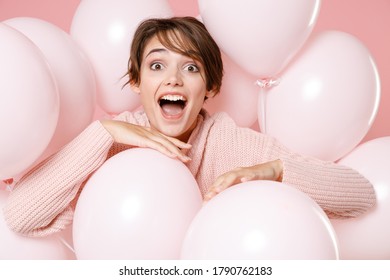Excited young brunette woman girl in knitted casual sweater posing isolated on pastel pink background. Birthday holiday party people emotions concept. Celebrating hold air balloons keeping mouth open.