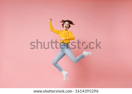 Excited young brunette woman girl in yellow sweater posing isolated on pastel pink background in studio. People lifestyle concept. Mock up copy space. Having fun fooling around, rising hands, jumping