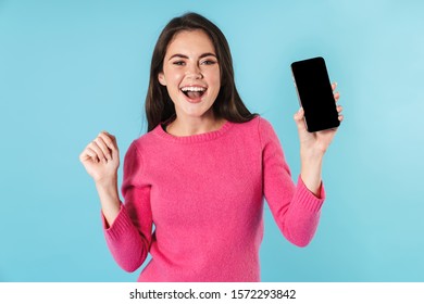 Excited Young Brunette Woman Standing Isolated Over Blue Background, Showing Blank Screen Mobile Phone, Celebrating