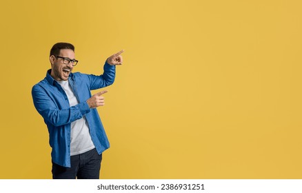 Excited young businessman screaming and pointing at empty space for marketing over yellow background - Powered by Shutterstock