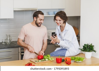 Excited young couple friends guy girl sit on table preparing vegetable salad cooking food in light kitchen at home. Dieting family healthy lifestyle concept. Using mobile phone - Powered by Shutterstock