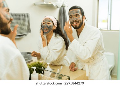 Excited young couple laughing having fun while putting on face mud mask and doing their skin care routine together - Powered by Shutterstock