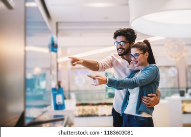 Excited Young Couple Looking At Big TV Screen For Their New Home.at Tech Store